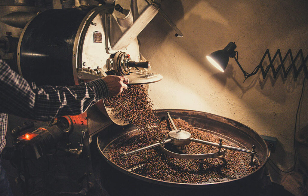 Un travailleur surveille la torréfaction des grains de café dans une machine industrielle, assurant une cuisson uniforme pour un arôme optimal.