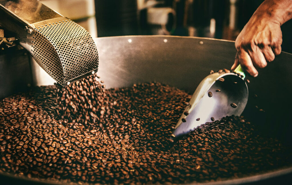 Un travailleur mélange les grains de café dans une grande cuve pour assurer une torréfaction homogène et une qualité constante.